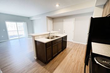 An empty kitchen and living room with wood flooring and a window